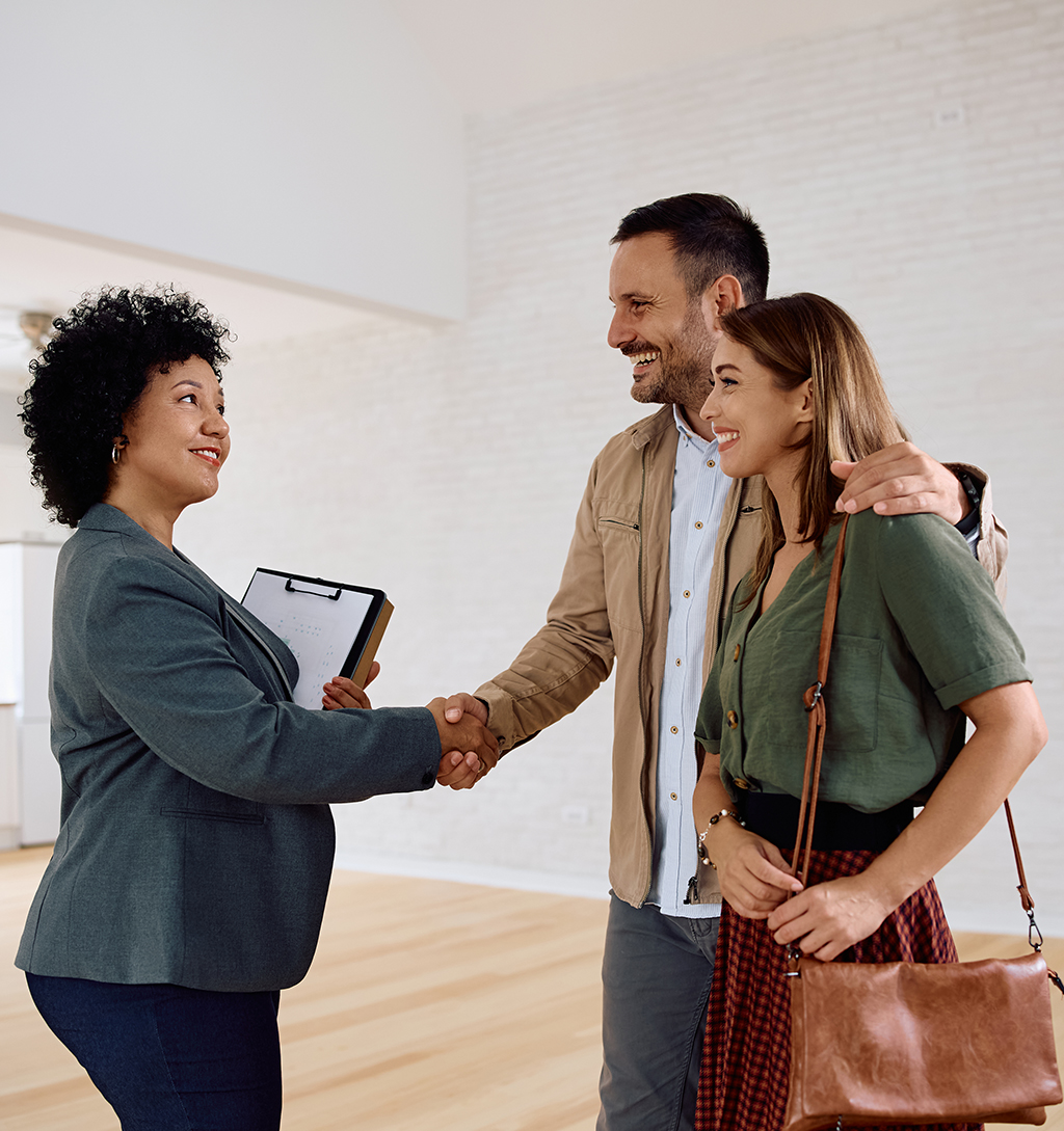 Happy couple and their real estate agent shaking hands in a new house.